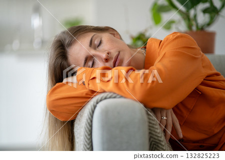 Middle-aged woman deeply tired and asleep on home sofa due to emotional exhaustion and fatigue 132825223