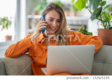 Excited middle-aged woman simultaneously using laptop and talking on phone gossiping with friend Excited middle-aged woman simultaneously using laptop and talking on phone gossiping with friend 132825239