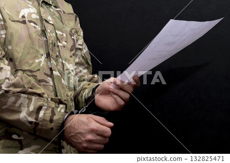a military man in a camouflage uniform is handcuffed, holding a white sheet of paper in his hand. Concept: military tribunal, the last word of the defendant, army court. 132825471