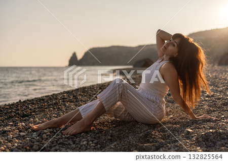 Woman beach sunset. Young woman relaxing on pebble beach at golden hour, enjoying the peaceful nature and warm light Woman beach sunset. Young woman relaxing on pebble beach at golden hour, enjoying the peaceful nature and warm light 132825564