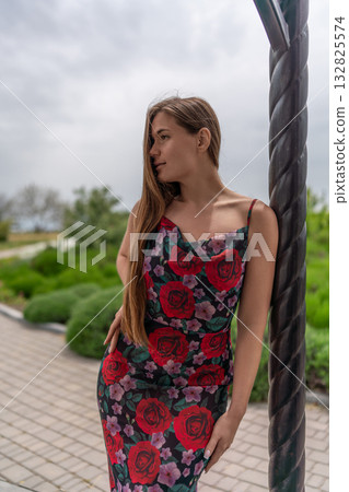 Woman floral dress park. Beautiful young woman in summer dress leaning against column looking away 132825574