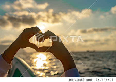 Hands heart sunset, creating a romantic shape against a beautiful golden ocean horizon. 132825594