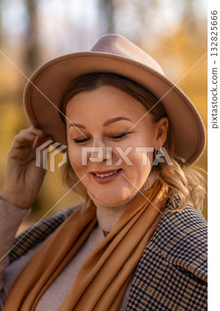 Woman Hat Autumn; Portrait, smiling woman adjusts hat outdoors during fall; golden hour lighting enhances mood. Woman Hat Autumn; Portrait, smiling woman adjusts hat outdoors during fall; golden hour lighting enhances mood. 132825666