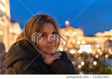 Woman city lights night portrait smiling wearing winter jacket against bright blurred urban skyline. 132825853