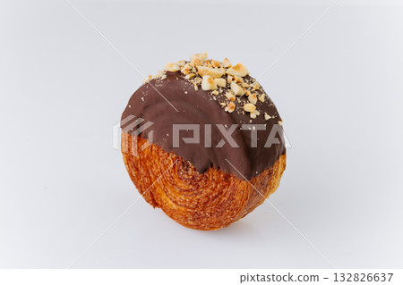 Round croissant pastry coated with chocolate glaze and crushed hazelnuts on white background 132826637