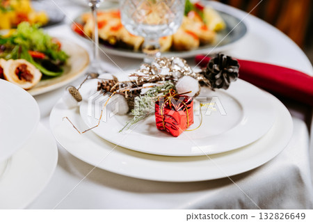 Elegant holiday table setting with festive decoration and small red gift box on plate 132826649