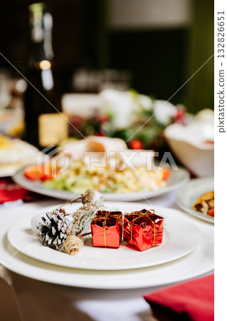 Elegant festive table setting with Christmas decor, white plates, and red gift accent 132826651