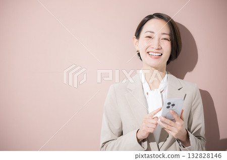 一位穿著西裝的女子正在用智慧型手機找東西,她對著鏡頭,背景是粉紅色的。 一位穿著西裝的女子正在用智慧型手機找東西,她對著鏡頭,背景是粉紅色的。 132828146