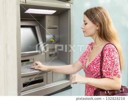 Woman uses ATM, withdraws cash from card. Girl buys travel ticket from machine Woman uses ATM, withdraws cash from card. Girl buys travel ticket from machine 132828210