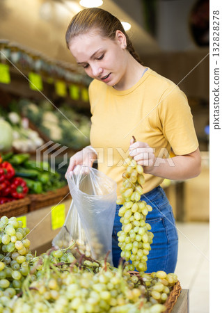 Girl selects ripe grapes from counter in grocery store 132828278