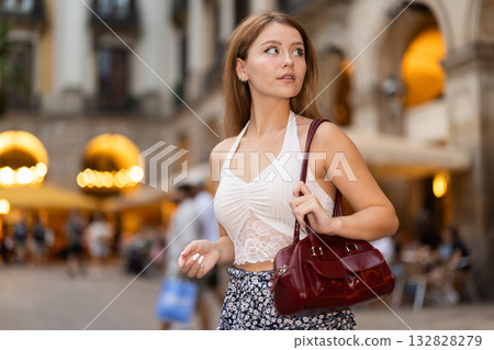 Woman in summer dress walks along the evening street of Barcelona against the backdrop of cafes and restaurants with romantic lighting 132828279