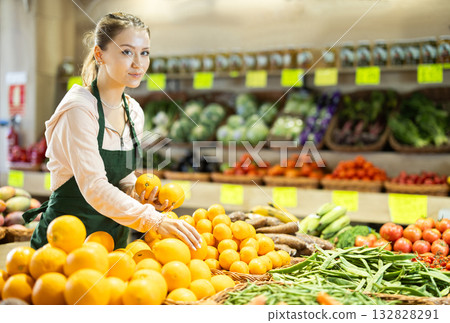 Young woman seller puts oranges in vegetable shop Young woman seller puts oranges in vegetable shop 132828291
