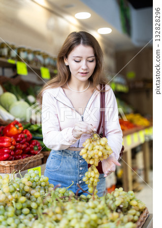 Girl selects ripe grapes from counter in grocery store 132828296