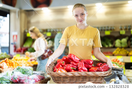 Teenage girl seller puts pepper in vegetable shop 132828328