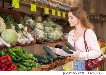 Young woman chooses cucumbers in store 132828330