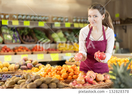 Young woman seller puts pomegranate in vegetable shop Young woman seller puts pomegranate in vegetable shop 132828378