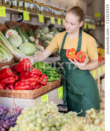 Woman employees in uniform holding fresh bell pepper in grocery shop 132828434