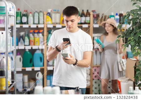 Guy buyer scans qr code on sunblock cream label, woman shopping in background 132828438