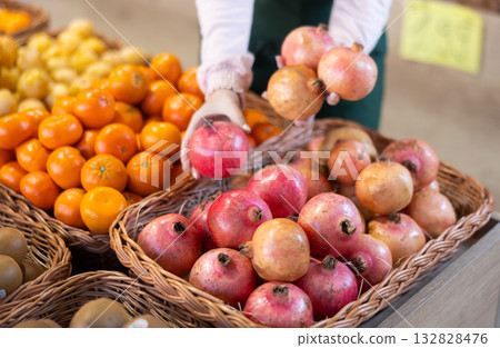 Saleswoman proposing pomegranate, offering fruits in supermarket Saleswoman proposing pomegranate, offering fruits in supermarket 132828476