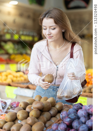 Woman chooses ripe kiwi for purchase in greengrocer shop 132828498