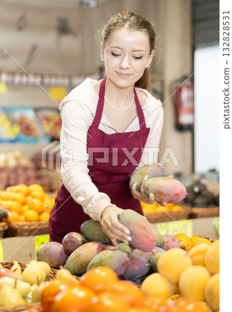 Girl employees in uniform holding mango in grocery shop Girl employees in uniform holding mango in grocery shop 132828531