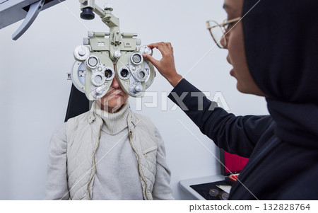 Eye exam, vision and woman with Muslim optometrist in clinic for test, eyesight and optical assessment. Optometry, healthcare and optician with elderly patient on phoropter, lens and medical machine Eye exam, vision and woman with Muslim optometrist in clinic for test, eyesight and optical assessment. Optometry, healthcare and optician with elderly patient on phoropter, lens and medical machine 132828764