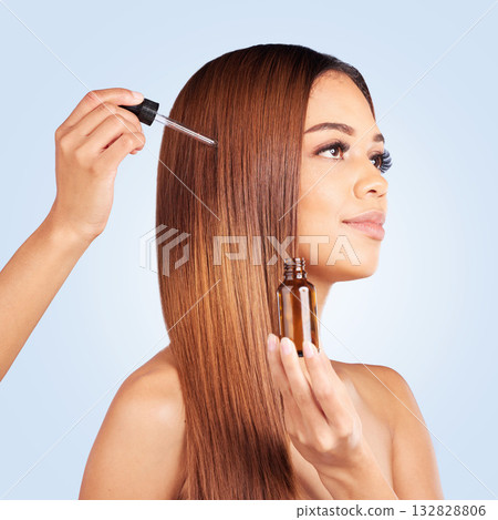 Beauty, hair care and woman with serum in studio isolated on a blue background. Cosmetics, thinking and female model apply hyaluronic acid, essential oil or hairstyle moisturizer for salon treatment. Beauty, hair care and woman with serum in studio isolated on a blue background. Cosmetics, thinking and female model apply hyaluronic acid, essential oil or hairstyle moisturizer for salon treatment. 132828806