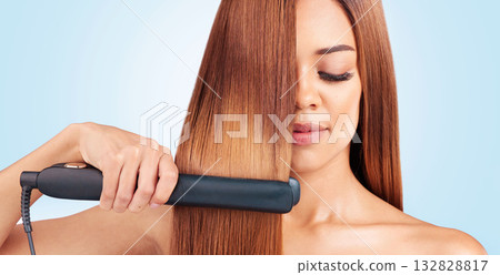 Face, beauty and woman with hair straightener in studio isolated on a blue background. Haircare, wellness and young female model with flat iron for salon treatment hairstyle, aesthetic or balayage. 132828817