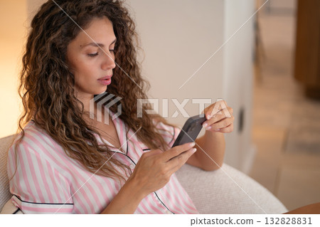 Woman in pajamas holding smartphone and reading 132828831