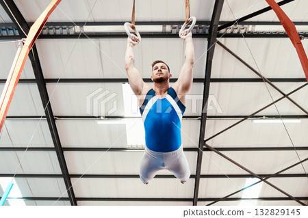 Man, acrobat and gymnastics swinging on rings in fitness for practice, training or workout at gym. Professional male gymnast hanging on ring circles for athletics, acrobatics or strength exercise 132829145
