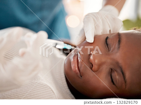 Face, syringe and skincare, black woman at spa with collagen injection for skincare and beauty treatment. Dermatology, cosmetics and person at salon with needle in skin for anti aging facial process. Face, syringe and skincare, black woman at spa with collagen injection for skincare and beauty treatment. Dermatology, cosmetics and person at salon with needle in skin for anti aging facial process. 132829170