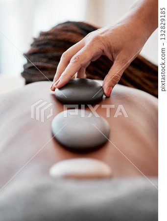 Black woman, hands and rock on back in spa treatment for relaxation, stress relief or massage at resort. Hand of masseuse applying rocks to African American female in physical therapy for wellness Black woman, hands and rock on back in spa treatment for relaxation, stress relief or massage at resort. Hand of masseuse applying rocks to African American female in physical therapy for wellness 132829185