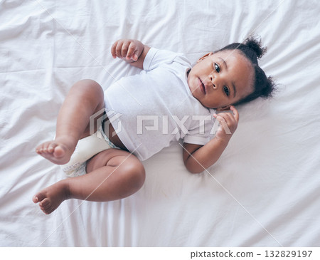 Baby, portrait and girl on a bedroom bed feeling relax and calm in a nursery after rest. Young newborn, child and kid with a diaper in the morning with wellbeing and childcare from above in a house 132829197