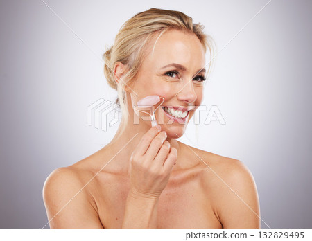 Face, massage and skincare with a mature woman in studio on a gray background for antiaging treatment. Beauty, relax and product with an attractive female massaging her skin for self care results Face, massage and skincare with a mature woman in studio on a gray background for antiaging treatment. Beauty, relax and product with an attractive female massaging her skin for self care results 132829495