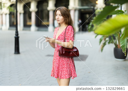 Girl in summer dress walks along street of the old town with mobile phone in her hands 132829661