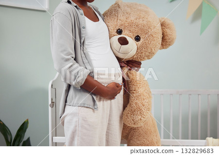 Pregnant, teddy bear and woman with hand on stomach for growth, development and bonding in room. Black person during pregnancy with stuffed animal toy for care, love and support for healthy lifestyle Pregnant, teddy bear and woman with hand on stomach for growth, development and bonding in room. Black person during pregnancy with stuffed animal toy for care, love and support for healthy lifestyle 132829683