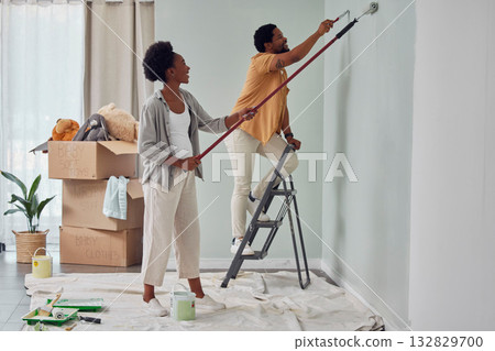 Painting, teamwork or black couple home renovation, diy or house remodel together with paintbrush or roller. Happy smile, woman and African man love working on wall with partnership or collaboration 132829700