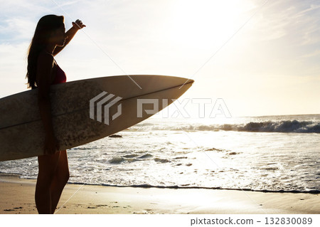 Silhouette, woman surfer on beach with sea and exercise outdoor with surfboard to surf in nature. Sport, shadow and sun with female person looking at ocean waves view with surfing and fitness Silhouette, woman surfer on beach with sea and exercise outdoor with surfboard to surf in nature. Sport, shadow and sun with female person looking at ocean waves view with surfing and fitness 132830089
