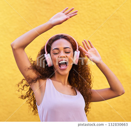 Music, freedom and dance with a black woman listening to the radio outdoor on a yellow wall background. Headphones, energy and face with an attractive young female streaming audio sound for fun Music, freedom and dance with a black woman listening to the radio outdoor on a yellow wall background. Headphones, energy and face with an attractive young female streaming audio sound for fun 132830663