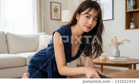 A woman in a navy blue dress smiling and holding a remote control in the living room A woman in a navy blue dress smiling and holding a remote control in the living room 132832433