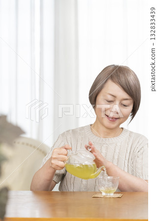 Senior woman drinking iced tea in the living room in summer Senior woman drinking iced tea in the living room in summer 132833439