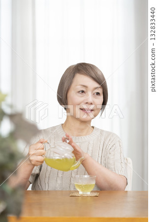 Senior woman drinking iced tea in the living room in summer 132833440
