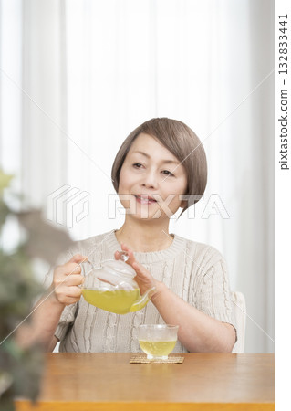 Senior woman drinking iced tea in the living room in summer Senior woman drinking iced tea in the living room in summer 132833441