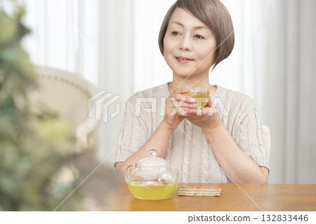 Senior woman drinking iced tea in the living room in summer 132833446
