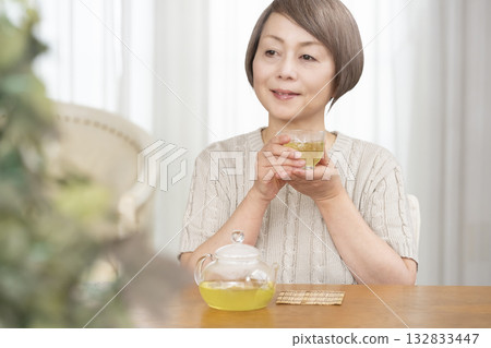 Senior woman drinking iced tea in the living room in summer Senior woman drinking iced tea in the living room in summer 132833447