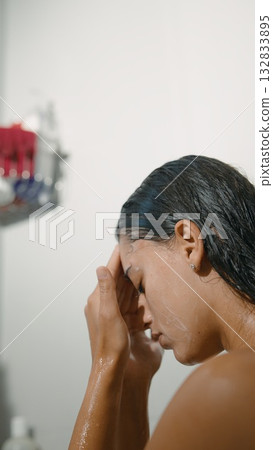 A woman is washing her hair in the shower while wearing a relaxed expression on her face 132833895