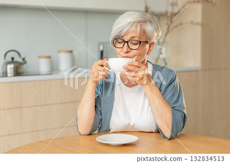 Good morning. Comfort relaxed senior old elderly woman grandmother drinking hot beverage tea coffee in kitchen at home. Mature woman resting enjoy calm morning at modern home alone. Pension concept Good morning. Comfort relaxed senior old elderly woman grandmother drinking hot beverage tea coffee in kitchen at home. Mature woman resting enjoy calm morning at modern home alone. Pension concept 132834513