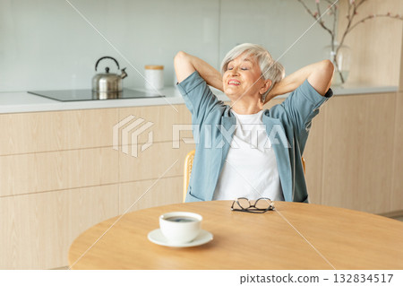 Senior old woman feeling relaxed stretching arms in kitchen at home. Smiling mature woman stretching hands feel positive optimistic fresh on bright morning new day. Good mood happy elderly lifestyle Senior old woman feeling relaxed stretching arms in kitchen at home. Smiling mature woman stretching hands feel positive optimistic fresh on bright morning new day. Good mood happy elderly lifestyle 132834517