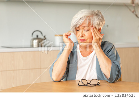 Headache pain. Unhappy middle aged senior woman suffering from headache sick rubbing temples at home. Mature old senior grandmother touching temples experiencing stress Woman feeling pain hurt in head Headache pain. Unhappy middle aged senior woman suffering from headache sick rubbing temples at home. Mature old senior grandmother touching temples experiencing stress Woman feeling pain hurt in head 132834525