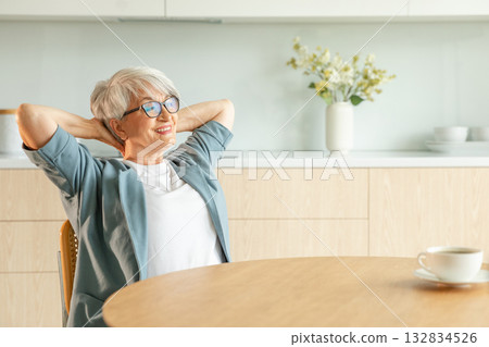 Senior old woman feeling relaxed stretching arms in kitchen at home. Smiling mature woman stretching hands feel positive optimistic fresh on bright morning new day. Good mood happy elderly lifestyle 132834526